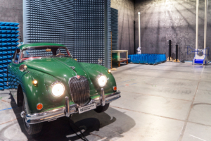 Jaguar XK150 in einer Prüfhalle. Die Prüfhalle ist mit Absorbern ausgestattet, im Hintergrund sieht man die Antenne, welche die elektromagnetischen Strahlen misst.