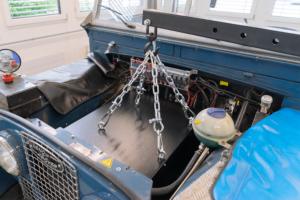 Einbau der Batteriekiste in den ehemaligen Motorraum des eLandys. Die Kiste ist an vier Haken mit Ketten an einem Kran befestigt und wird so hineingehoben.