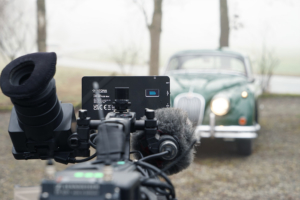 Eine Kamera von hinten aufgenommen, wie sie auf den Jaguar XK 150 ausgerichtet ist. Im Hintergrund neblige Landschaft