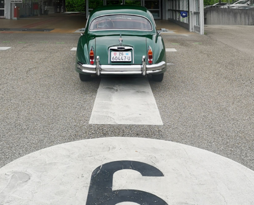 Ein grüner Jaguar XK 150 steht auf einer Prüfbahn des Strassenverkehrsamtes Zug. Ansicht von Hinten auf das Auto. Man erkennt die Bahnnummer 6 im Bild unten, etwas angeschnitten.