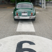 Ein grüner Jaguar XK 150 steht auf einer Prüfbahn des Strassenverkehrsamtes Zug. Ansicht von Hinten auf das Auto. Man erkennt die Bahnnummer 6 im Bild unten, etwas angeschnitten.