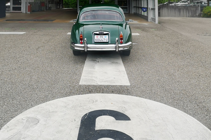 Ein grüner Jaguar XK 150 steht auf einer Prüfbahn des Strassenverkehrsamtes Zug. Ansicht von Hinten auf das Auto. Man erkennt die Bahnnummer 6 im Bild unten, etwas angeschnitten.