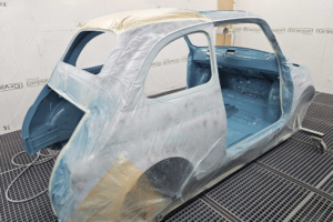 Ein Fiat 500 in einer Lackierkabiene. Die Aussenseite ist mit Folie abgedeckt, der Innenraum ist in Wagenfarbe, also mittelblau, lackiert.