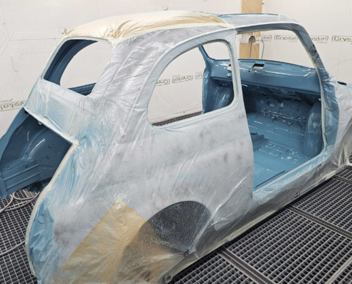 Ein Fiat 500 in einer Lackierkabiene. Die Aussenseite ist mit Folie abgedeckt, der Innenraum ist in Wagenfarbe, also mittelblau, lackiert.