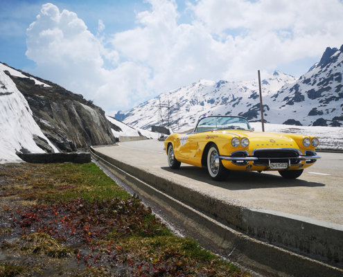 Corvette on Gotthard mountain road Eine gelbe Corvette ist am Rande einer Passstrasse parkiert. Links hat es einen Schneewall, im Hintergrund eine leicht verschneite Berglandschaft.