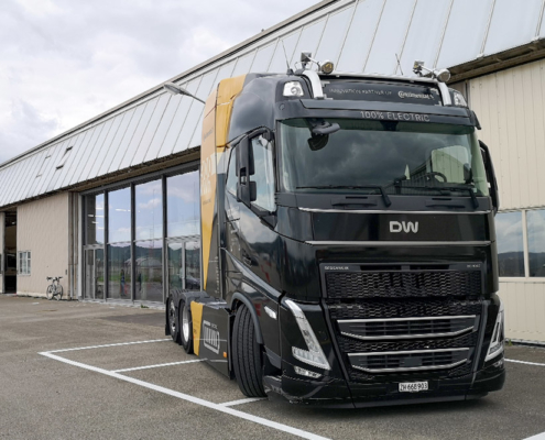 Designwerk-LKW Ein schwarzes Zugfahrzeug steht vor einem Hangar. Vorne am Fahrzeug das Logo der Firma Designwerk.