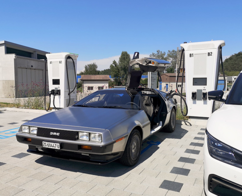 144719_manufakturmarton_ladedose_blog Delorean wird an der Ladesäule geladen. Ansicht des ganzen Fahrzeugs, leicht schräg.