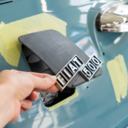Ladeklappe, noch roh und schwarz, mit originalem Fiatschriftzug für den elektrifizierten Fiat 500. Eine Hand hält sie etwas offen.