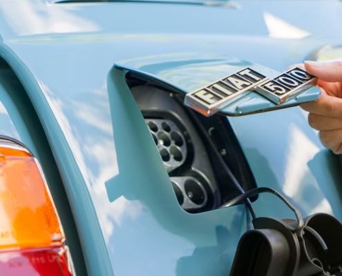 The finished charging flap Eine Öffnung am Heck des blau lackierten Fiat 500, die mit einer Klappe in Wagenfarbe verschlossen werden kann. Im Bild ist diese halb geöffnet, an ihr ist das Logo "Fiat 500" angebracht.
