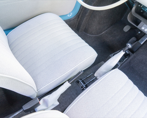 The colour and material scheme for the interior was also implemented in accordance with the customer’s wishes Mit hellem Stoff bezogene Fahrzeugsitze, von oben aufgenommen. Dazwischen diverse Hebel: Handbremse, Regler für die Temperatur, Schalthebel.