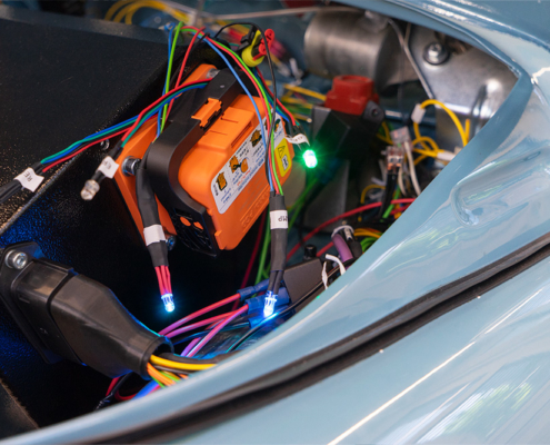 Preparations and testing of the LEDs to be fitted in the display Der Frontraum eines Fahrzeugs. Es sind diverse Kabel sichtbar, an einigen sind LEDs in verschiedenen Farben verbaut. An einer schwarzen Box, der Batteriekiste, ist ein oranger Trennschalter verbaut.