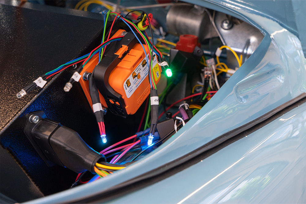 Preparations and testing of the LEDs to be fitted in the display Der Frontraum eines Fahrzeugs. Es sind diverse Kabel sichtbar, an einigen sind LEDs in verschiedenen Farben verbaut. An einer schwarzen Box, der Batteriekiste, ist ein oranger Trennschalter verbaut.