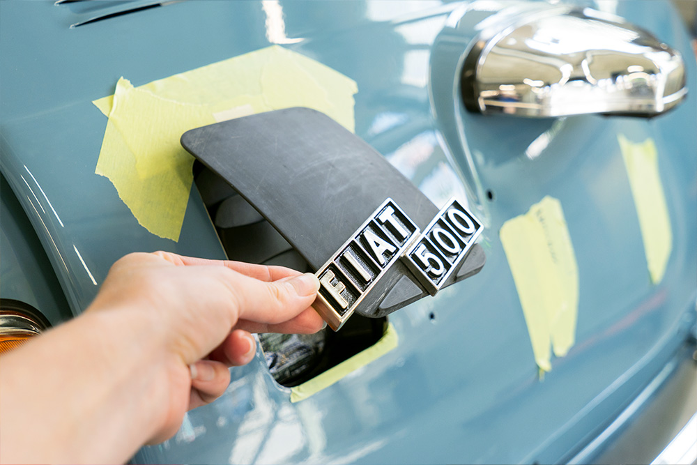 At the rear of the vehicle is a new charging flap, which is still in development Eine Öffnung am Heck des blau lackierten Fiat 500, die mit einer Klappe aus Kunststoff verschlossen werden kann. Im Bild ist diese halb geöffnet, an ihr ist das Logo "Fiat 500" angebracht.